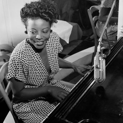 A black and white photo of Mary Lou Williams playing the piano