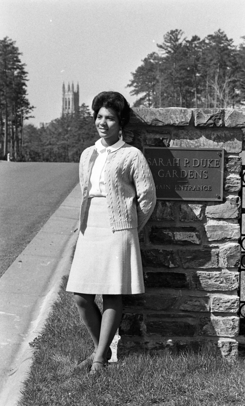 Wilhelmina Reuben-Cooke standing in front of the Sarah P. Duke Gardens entrance plaque with Duke Chapel in the background.