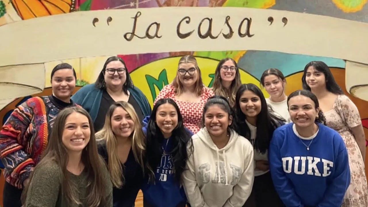 A group of students stand with their professor in front of a mural