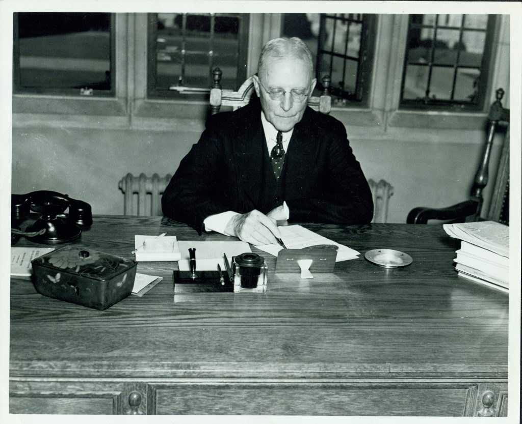 Flowers working at his desk, pen in right hand