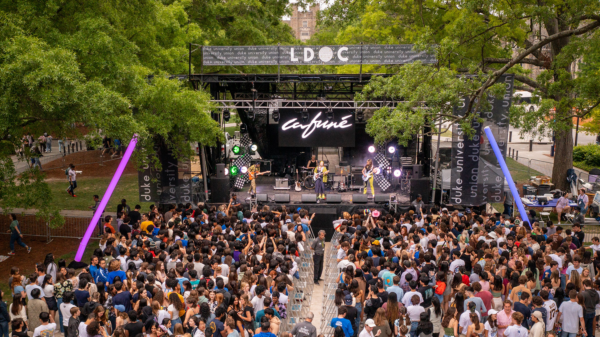 A recent photo of an LDOC concert with crowd and lights between large trees on the quad