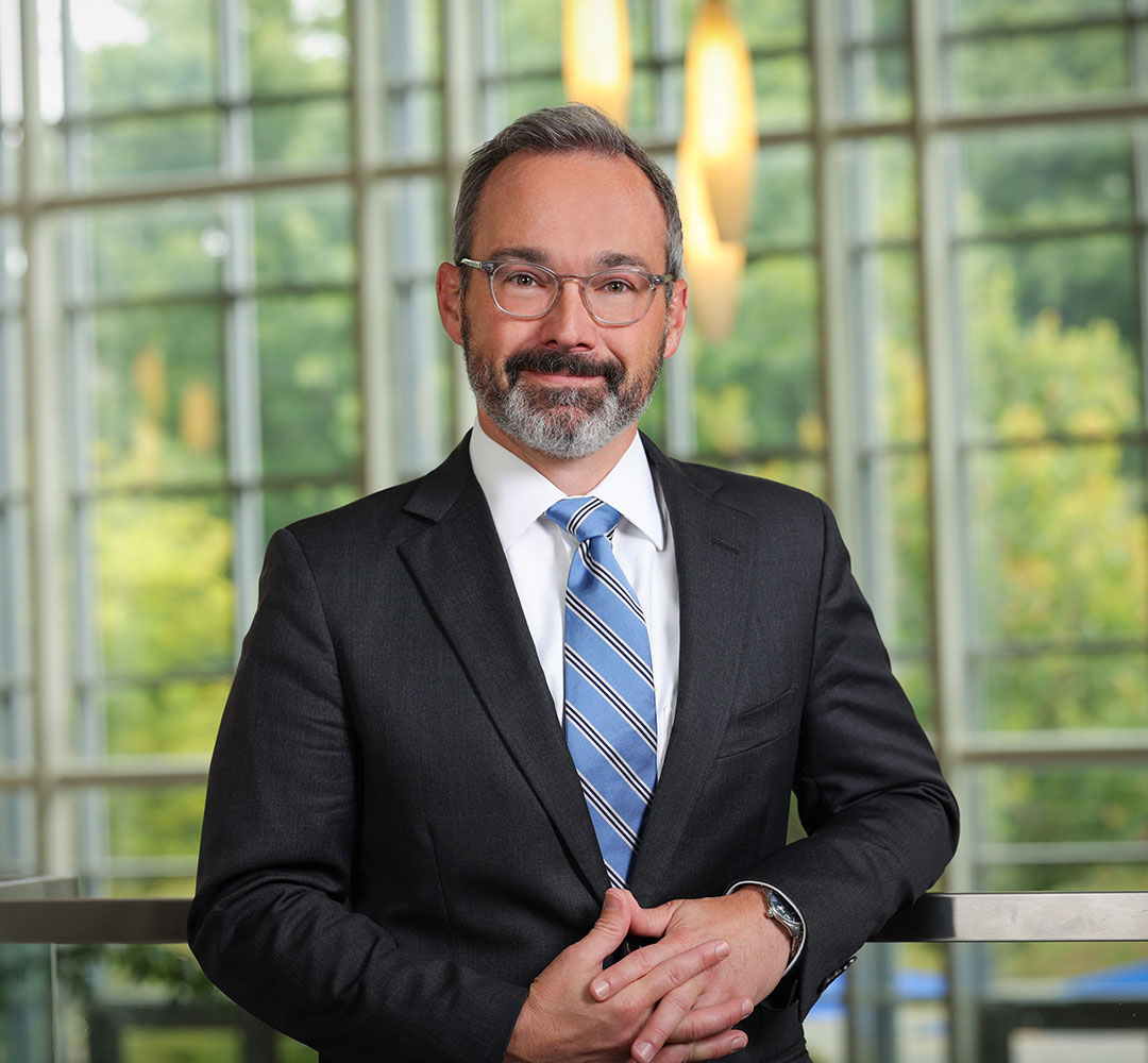 Joseph Blocher standing against a railing with windows in the background