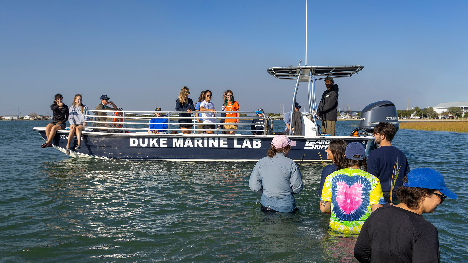 A color photo of students wading out to a very flat boat with Duke Marine Lab written on the side