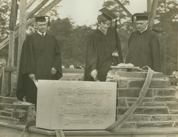 Doris Duke, in cap and gown, sets the cornerstone for West Campus