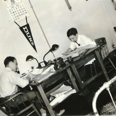 A historic photo of engineering students at Desks with a Duke penant on the wall