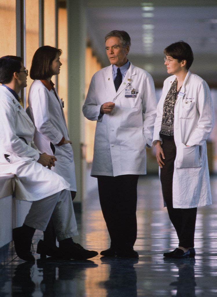 Ralph Snyderman in a white coat with residents in a hospital hallway