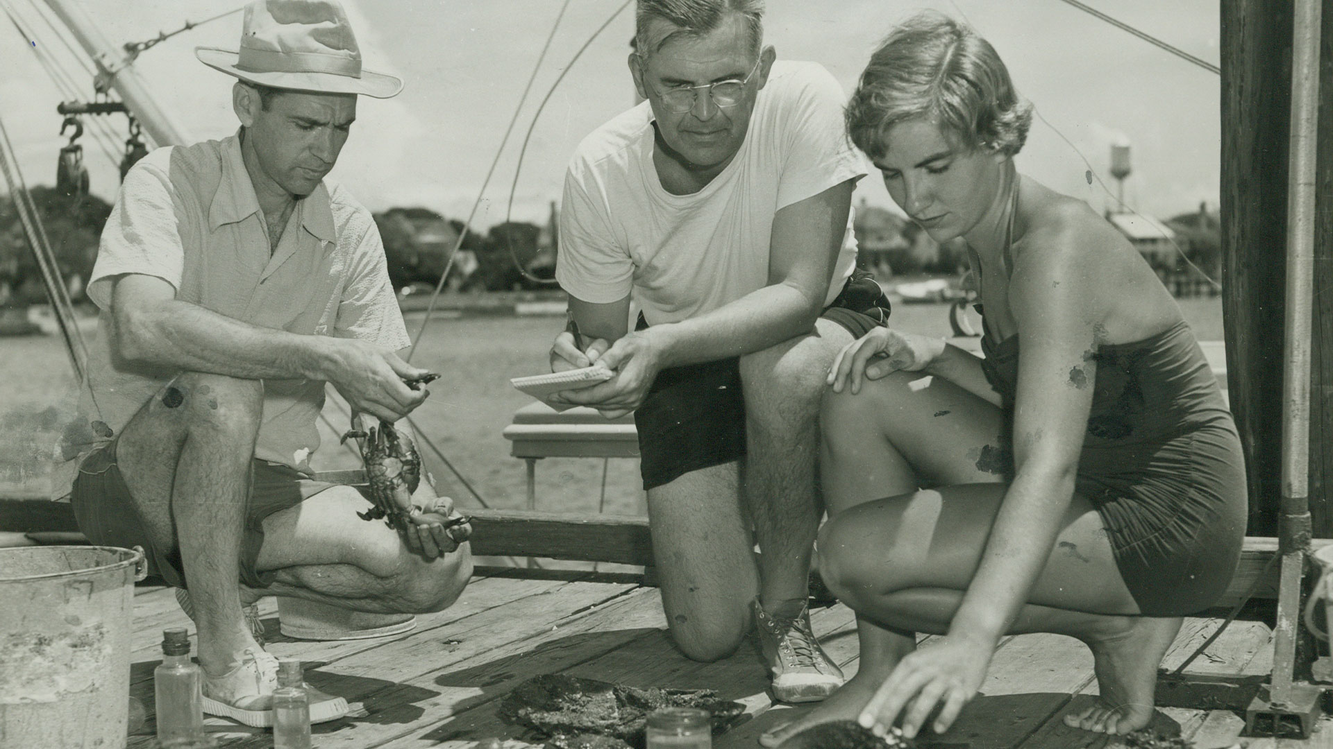 A black and white photo of people looking at items on a dock