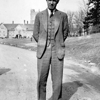 Wallace Wade stands on a dirt road on West Campus with the clocktower in the background