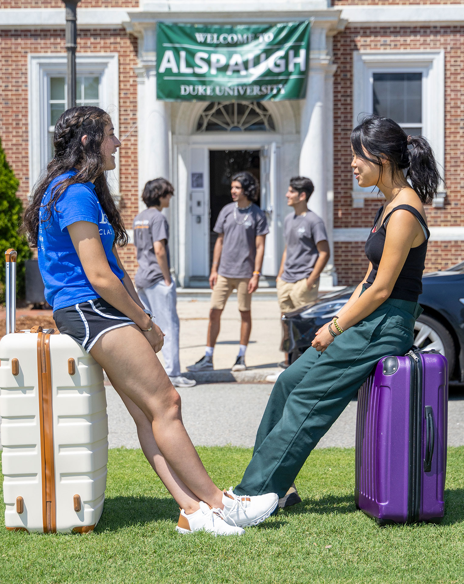 An recent photo of two women sit on suitcases in front of Alspaugh on Move-in day