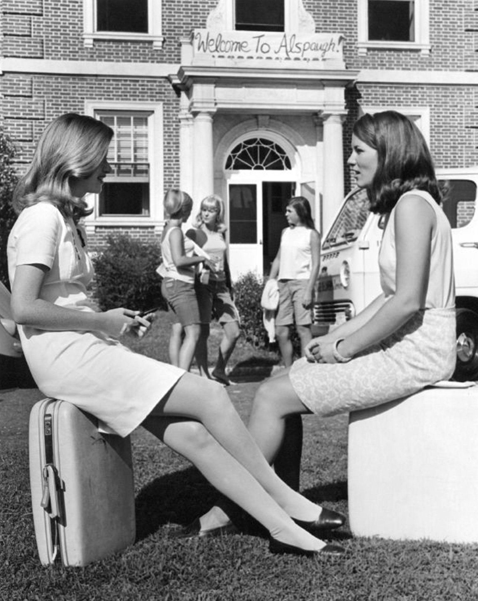 An old photo of two women sit on suitcases in front of Alspaugh on Move-in day