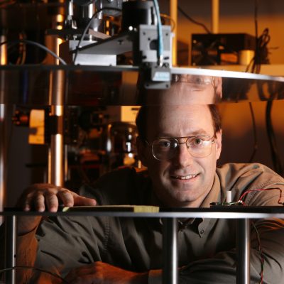 David Smith peers, smiling, between two shelves housing lab equipment