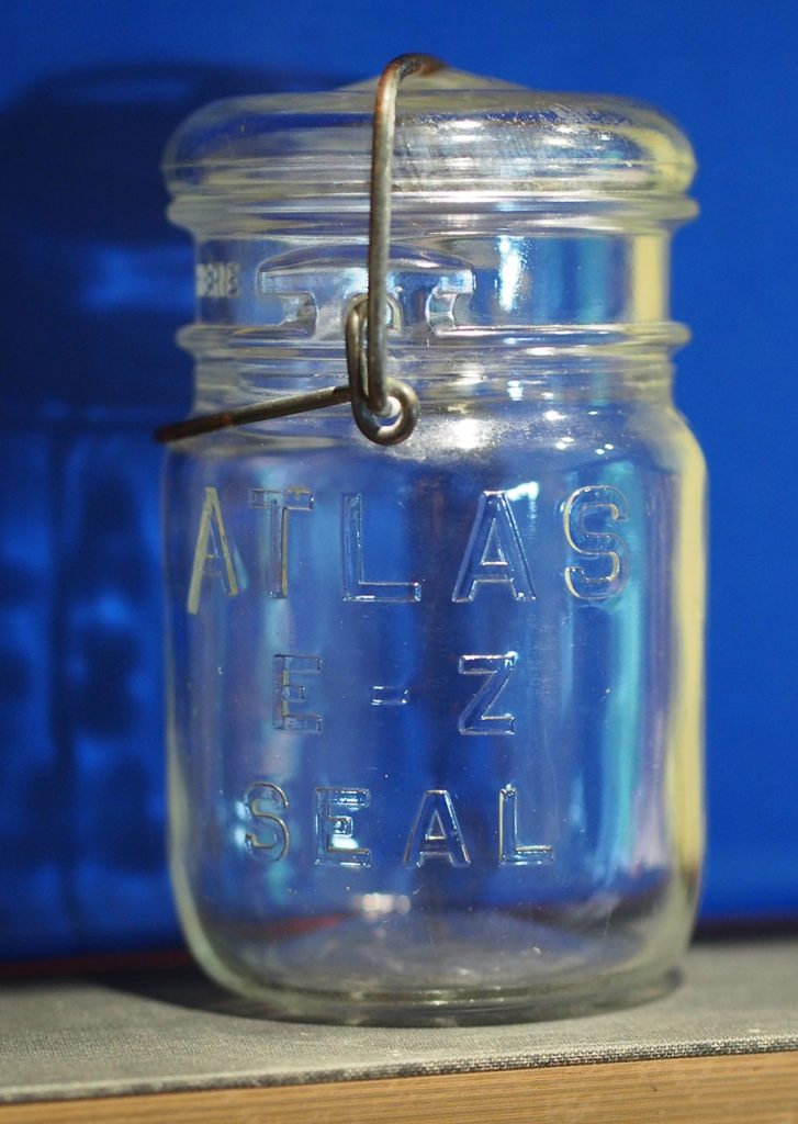 A glass canning jar that says "ATLAS E - Z SEAL" in front of a blue background